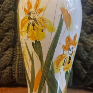 Può includere: Vaso in ceramica bianca con design floreale giallo e arancione dipinto a mano. Il vaso presenta foglie verdi e dettagli dorati. È un oggetto decorativo, adatto per esporre fiori o come pezzo unico.