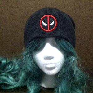 May include: Black knit beanie with a red and white Deadpool logo embroidered on the front.