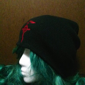 May include: Black beanie with a red embroidered symbol on the front. The symbol is a stylized kanji character.