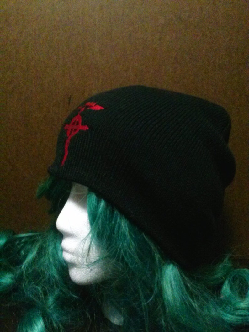 May include: Black beanie with a red embroidered symbol on the front. The symbol is a stylized kanji character.