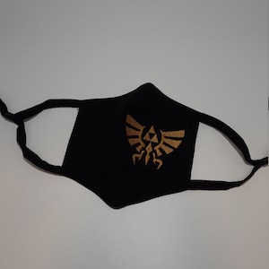 May include: Black face mask with a gold embroidered Triforce symbol from the Legend of Zelda video game series.