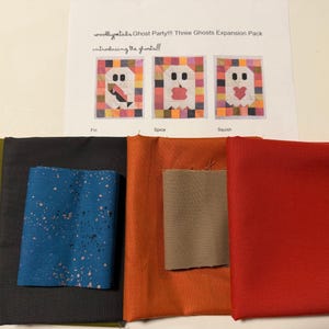 May include: A collection of fabric swatches in solid colors including red, orange, olive green, dark gray, and a blue piece with speckles, accompanied by a printed instruction sheet titled "woollypetals Ghost Party!!! Three Ghosts Expansion Pack".