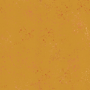 May include: Mustard-colored fabric with a speckled pattern. The fabric features small, irregular spots in shades of pink and red scattered across the surface. The overall effect is a textured, artistic design suitable for various craft projects.