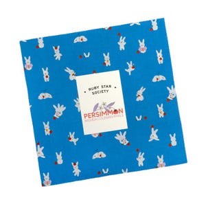 May include: A square piece of bright blue fabric featuring a repeating pattern of small white rabbits in various poses. A white paper label is centered on the fabric with the text Ruby Star Society, Persimmon, and Rashida Coleman Hale printed on it.