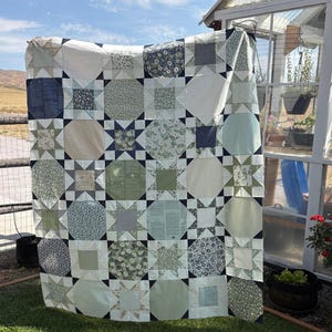 May include: A quilt featuring a repeating pattern of octagonal shapes and star blocks. The fabric displays various shades of green, white, and navy blue, with diverse floral, geometric, and text-based prints arranged in a grid across the surface.