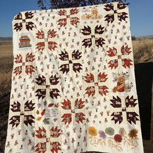 May include: A patchwork quilt featuring a cream background with repeating blocks of dark brown bear paw patterns and fabric squares printed with autumn leaves, pumpkins, sunflowers, and coffee mugs, along with text panels reading Hello Pumpkin, Leaves are Falling, and more.