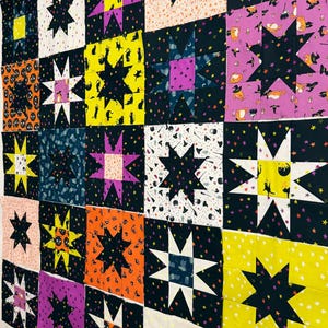 May include: A patchwork quilt top featuring a grid of star-patterned blocks. The fabric displays various Halloween-themed prints including black cats, witches, pumpkins, and stars in vibrant colors like yellow, orange, purple, black, and white.