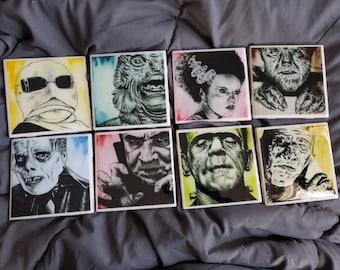 May include: Set of eight square ceramic coasters featuring black and white illustrations of classic horror movie monsters. The coasters have a watercolor background in various colors, including yellow, green, pink, and blue.