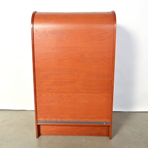 May include: A tall, wooden cabinet with a curved top and a sliding door. The cabinet is made of a light brown wood with a natural finish.