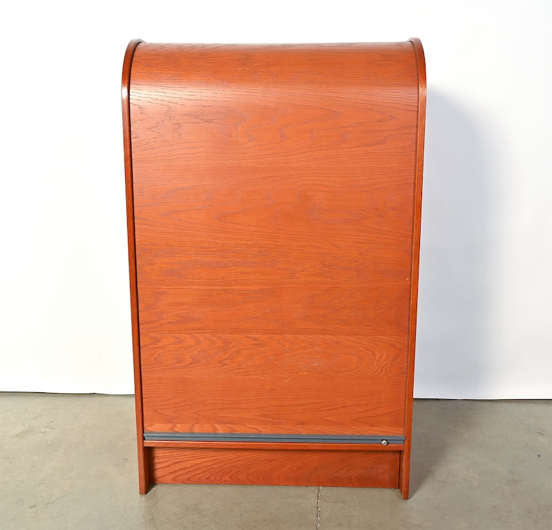 May include: A tall, wooden cabinet with a curved top and a sliding door. The cabinet is made of a light brown wood with a natural finish.
