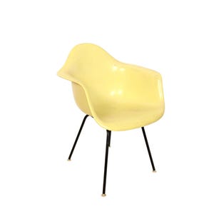 May include: A vintage yellow armchair with a curved seat and backrest. The chair has black metal legs and a minimalist design. The chair's dimensions are approximately 30 inches high, 25 inches wide, and 25 inches deep.