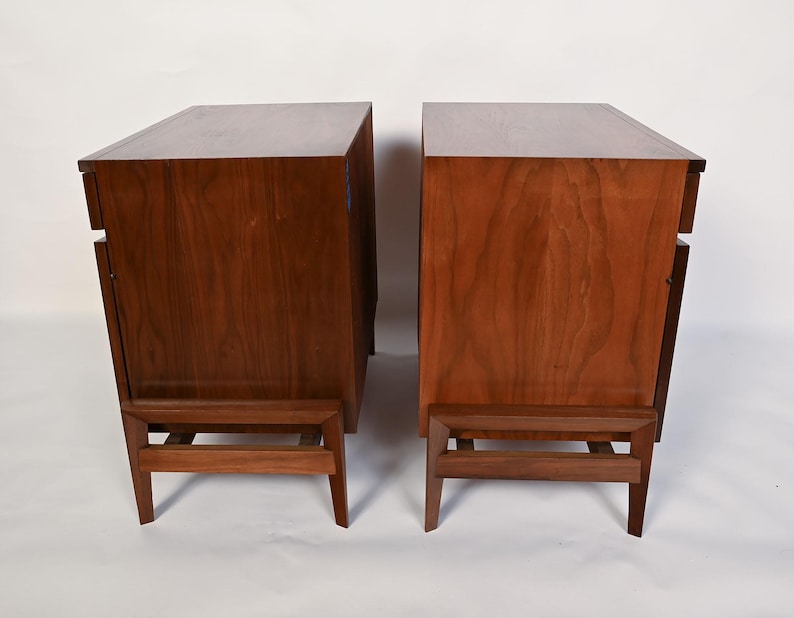 Puede incluir: Dos mesitas de noche de madera a juego con un acabado marr&oacute;n intenso. Cada mesita tiene un dise&ntilde;o rectangular, un caj&oacute;n y una estructura de patas &uacute;nica. La veta de la madera es visible, lo que a&ntilde;ade a la est&eacute;tica natural.