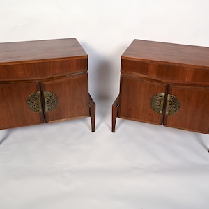 Puede incluir: Dos armarios de madera a juego con un acabado marr&oacute;n c&aacute;lido. Cada armario tiene dos puertas con un tirador circular de lat&oacute;n y se apoya en cuatro patas anguladas. Los armarios tienen un dise&ntilde;o moderno de mediados de siglo.