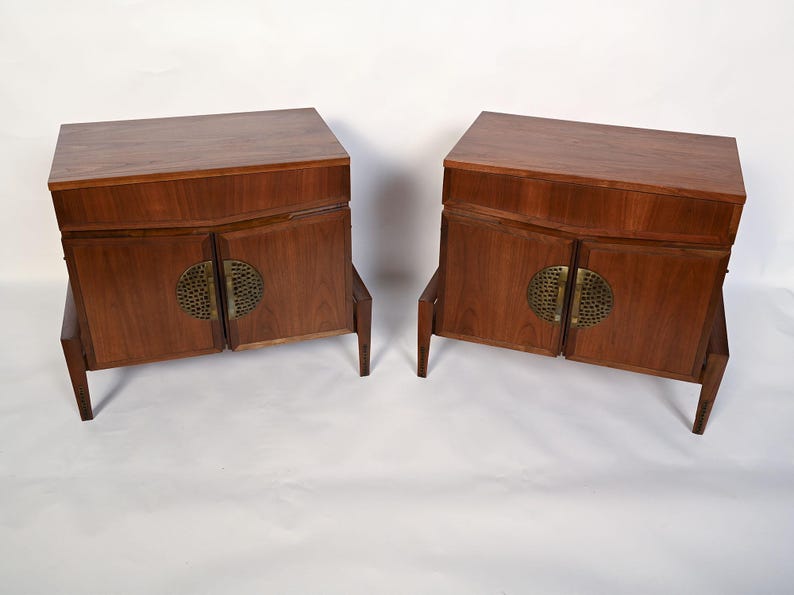 Puede incluir: Dos armarios de madera a juego con un acabado marr&oacute;n c&aacute;lido. Cada armario tiene dos puertas con un tirador circular de lat&oacute;n y se apoya en cuatro patas anguladas. Los armarios tienen un dise&ntilde;o moderno de mediados de siglo.
