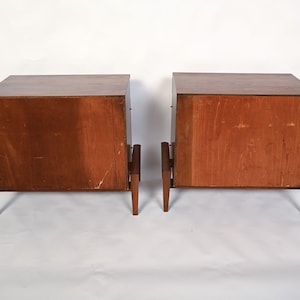 Puede incluir: Dos mesitas de noche de madera a juego con un acabado marr&oacute;n c&aacute;lido. Cada mesita de noche tiene un mueble rectangular con una parte superior plana y est&aacute; sostenida por cuatro patas delgadas e inclinadas. Las mesitas de noche est&aacute;n una al lado de la otra.