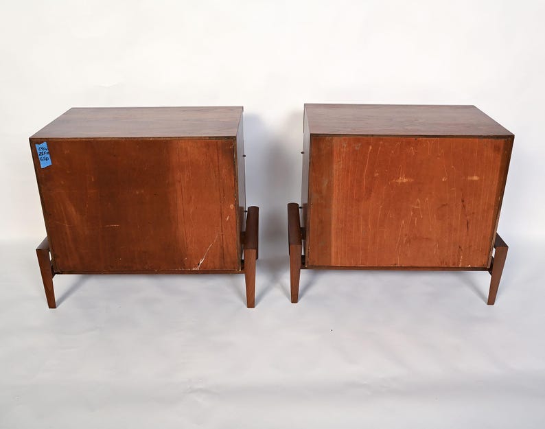 Puede incluir: Dos mesitas de noche de madera a juego con un acabado marr&oacute;n c&aacute;lido. Cada mesita de noche tiene un mueble rectangular con una parte superior plana y est&aacute; sostenida por cuatro patas delgadas e inclinadas. Las mesitas de noche est&aacute;n una al lado de la otra.