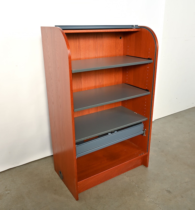 May include: A wooden cabinet with a curved front and a sliding door. The cabinet has four shelves and a drawer. The shelves are gray and the cabinet is a reddish-brown color.