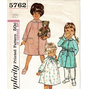 May include: Vintage Simplicity pattern 5762 for toddler size 3. The pattern features illustrations of three young children in various outfits, including a pink coat, a floral dress, and a blue checkered dress with white pants. The pattern includes the text "Printed Pattern 50c IN CANADA 60c".