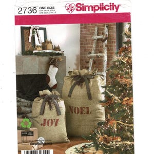 May include: Simplicity pattern 2736 for Christmas-themed burlap sacks. The sacks are tan with red text that reads "JOY" and "NOEL". The image also shows a Christmas tree, a fireplace, and a decorative ladder.