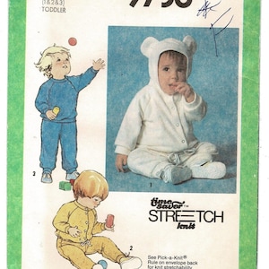 May include: A Simplicity 9738 sewing pattern envelope for toddler sizes K (1, 2, and 3). The cover features illustrations of children wearing a two-piece outfit and a white hooded jumpsuit with bear ears. Text includes Time Saver Stretch Knit.