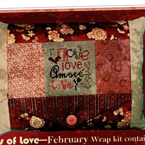 May include: A rectangular decorative pillow featuring a patchwork design with floral and striped fabrics in shades of red, pink, and cream. The center panel displays cross-stitched text reading "love" in multiple languages, including "amore".