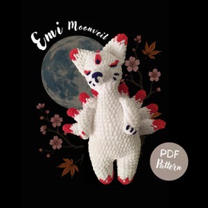 May include: A white crocheted fox-like plush toy with red accents on its ears and tails, set against a black background with a full moon and floral elements. The text "Emi Moonveil" is above the toy.