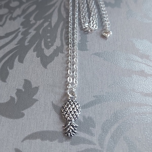 Può includere: Una collana con catena d'argento con un ciondolo a forma di ananas. La catena è di stile a cavo delicato. Il ciondolo a forma di ananas è dettagliato e ha una superficie testurizzata.