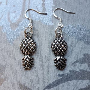 May include: A pair of silver pineapple earrings with a textured design. The earrings are on a white background.
