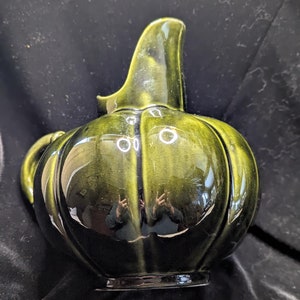 May include: A green ceramic pitcher with a rounded body and a curved spout. The pitcher has a glossy finish and a ribbed design.