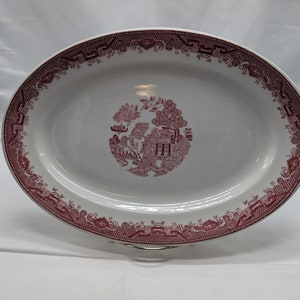 May include: A white oval serving platter with a pink willow pattern design. The pattern features a stylized tree, a house, and a bridge.