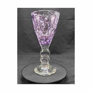 May include: A clear glass goblet with a purple and white swirl design. The goblet has a round base and a tall stem.