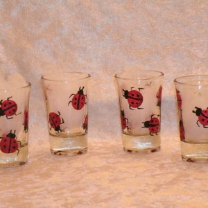 May include: Four clear glass shot glasses with red and black ladybug designs painted on them.