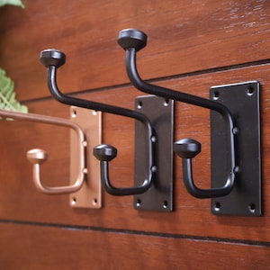 May include: Three wall-mounted hooks with a black finish and two with a copper finish. Each hook has a double-prong design.