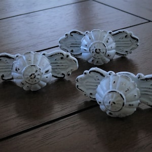 May include: Three white metal drawer pulls with a decorative floral design. The pulls have a distressed finish and are ideal for adding a touch of vintage charm to any home.