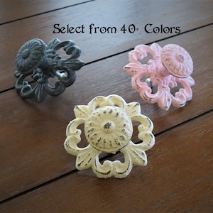 May include: Three decorative cabinet knobs with ornate floral designs. The knobs are in black, pink, and off-white. Select from 40+ Colors.