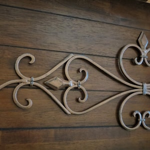 May include: A decorative metal wall decor with a scroll design in a gold finish. The design features a series of connected loops and swirls.