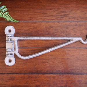 May include: A silver metal shelf bracket with a hook on the end. The bracket is attached to a wooden surface.