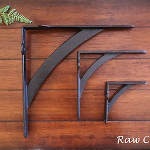 May include: Three black cast iron shelf brackets of different sizes, mounted on a wooden wall. The text "Raw Cast Iron" is visible at the bottom of the image.