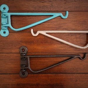 Puede incluir: Tres soportes de estantería metálicos en diferentes colores: turquesa, blanco y negro. Cada soporte tiene un gancho en el extremo y un diseño decorativo en el lateral.