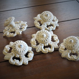 Op de afbeelding: Vijf witte keramische ladegrepen met ingewikkelde bloemmotieven en blauwe accenten. De grepen hebben een verweerde afwerking.