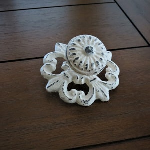 May include: White cast iron cabinet knob with a decorative floral design. The knob has a round, raised centre with a textured surface.