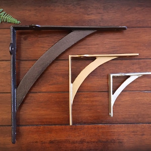 May include: Three metal shelf brackets in different sizes. The largest bracket is black, the middle bracket is gold, and the smallest bracket is silver.