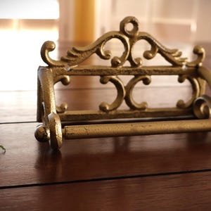 Puede incluir: Portarrollos de papel higi&eacute;nico de metal dorado de estilo antiguo y ornamentado. El soporte presenta volutas decorativas y una barra para sujetar el rollo de papel higi&eacute;nico. El accesorio est&aacute; dise&ntilde;ado para montarse en la pared.