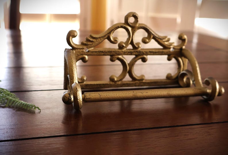 Puede incluir: Portarrollos de papel higi&eacute;nico de metal dorado de estilo antiguo y ornamentado. El soporte presenta volutas decorativas y una barra para sujetar el rollo de papel higi&eacute;nico. El accesorio est&aacute; dise&ntilde;ado para montarse en la pared.
