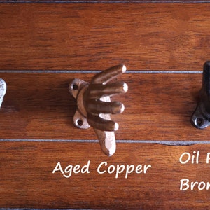 May include: Three hand-shaped hooks in different finishes: silver, aged copper, and oil rubbed bronze. The hooks are mounted on a wooden surface.