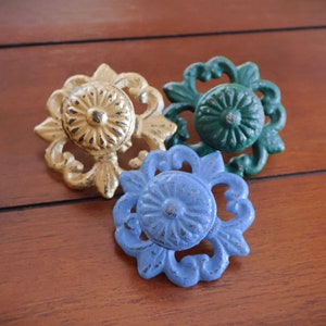 May include: Three decorative drawer pulls with ornate floral designs. The pulls are painted in gold, blue, and green.