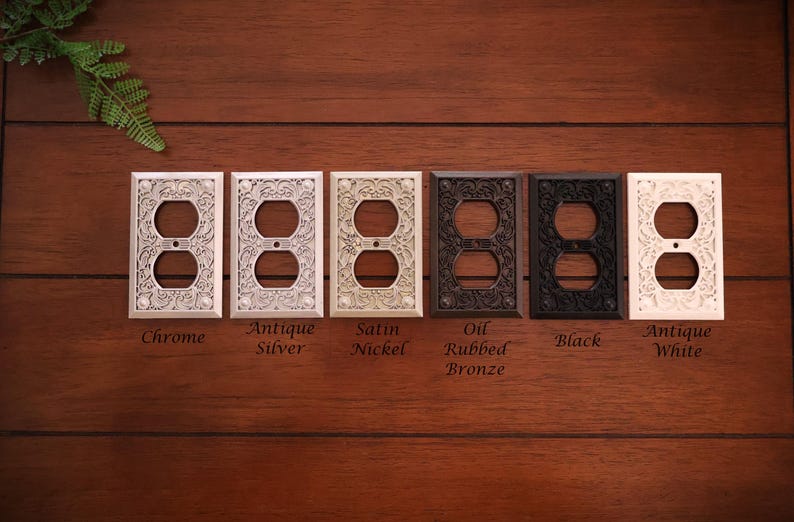 Puede incluir: Una colecci&oacute;n de cubiertas decorativas para enchufes el&eacute;ctricos en varios acabados, incluyendo cromo, plata antigua, n&iacute;quel satinado, bronce aceitado, negro y blanco antiguo. Cada cubierta presenta un dise&ntilde;o floral ornamentado.