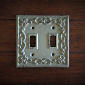 May include: A light green, decorative, double light switch cover with an ornate, floral design.