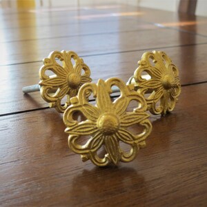 May include: Three gold-toned metal drawer pulls with a floral design. Each pull has a screw for attaching to a drawer.