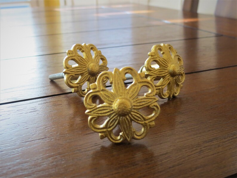 May include: Three gold-toned metal drawer pulls with a floral design. Each pull has a screw for attaching to a drawer.